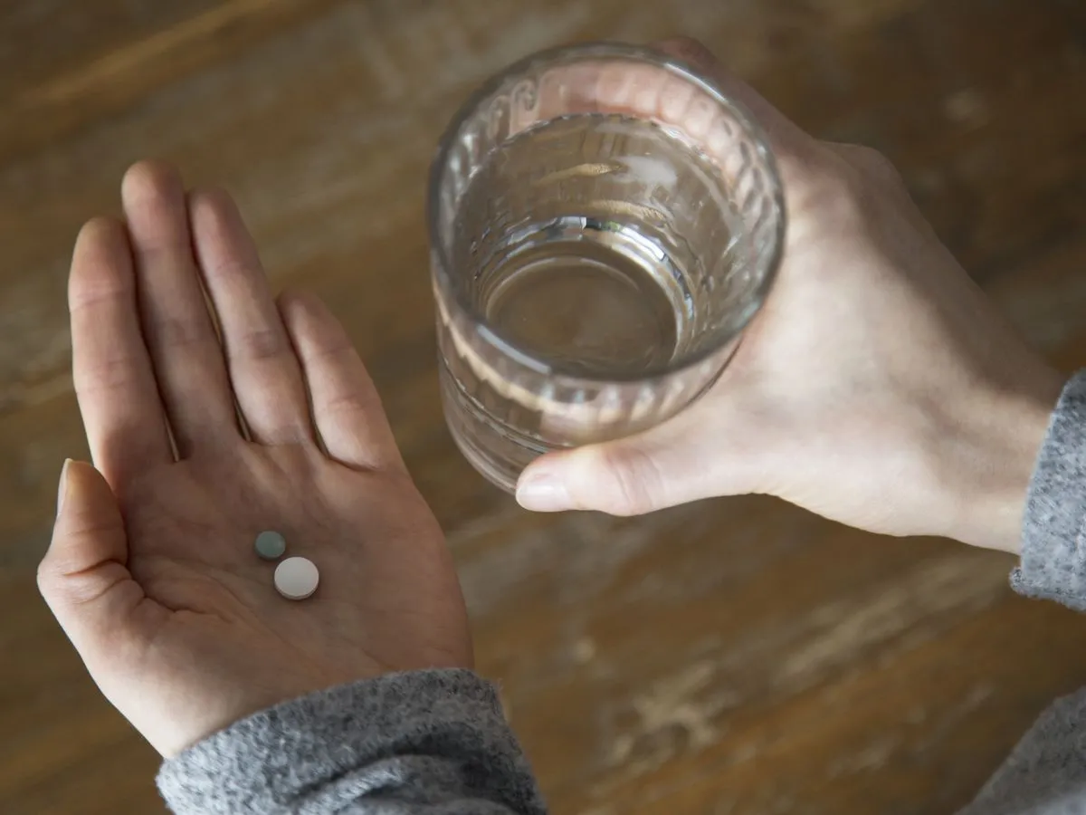 Zwei Tabletten in der Hand, daneben ein Glas Wasser