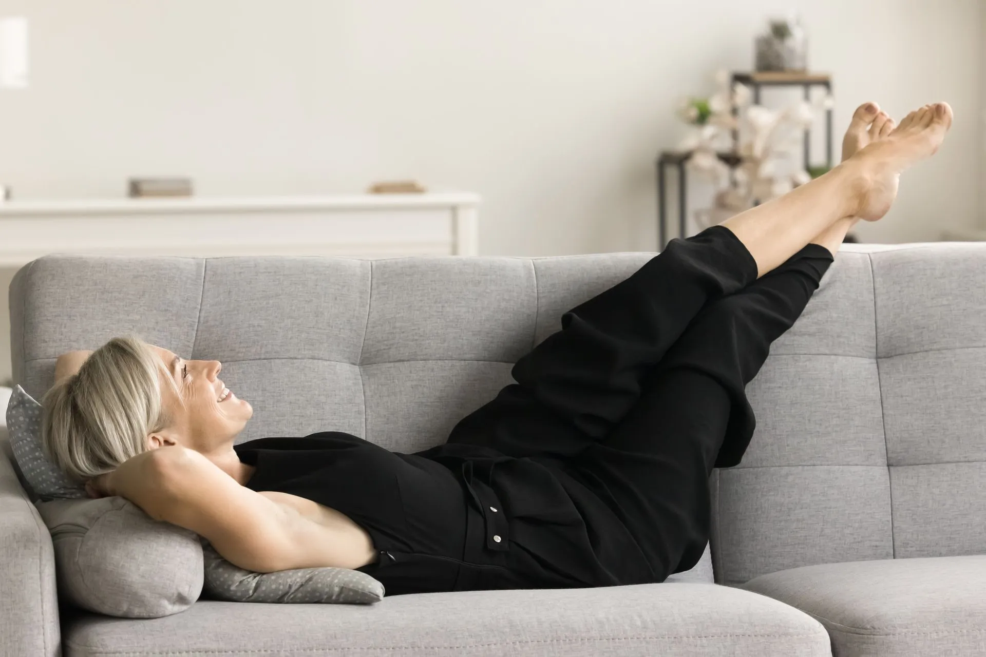 Frau liegt auf dem Sofa und legt die Beine hoch