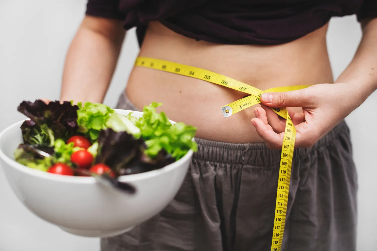 Frau mit Maßband um die Taille und einer Schüssel Salat