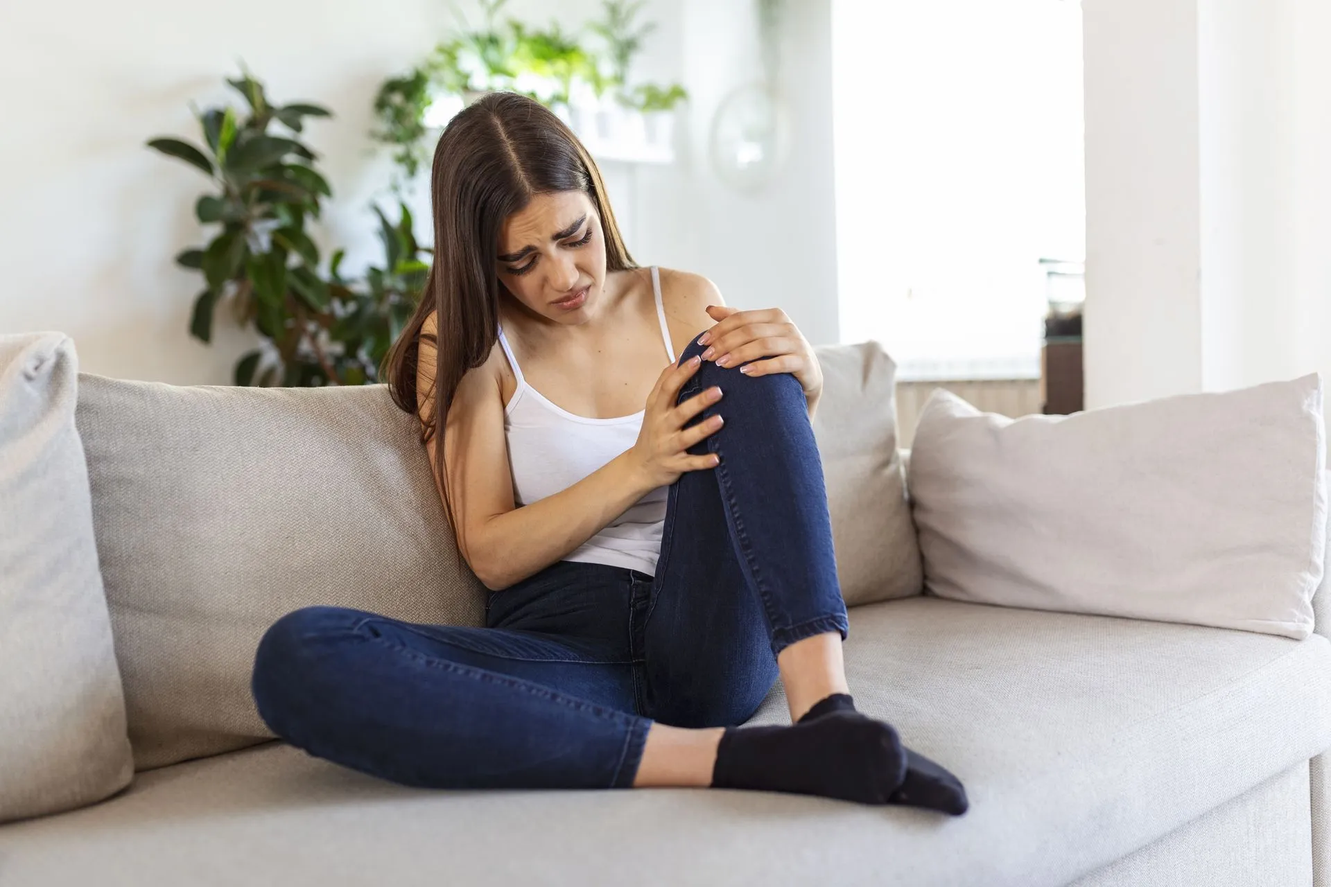 Frau sitzt auf dem Sofa und hält sich das schmerzende Knie